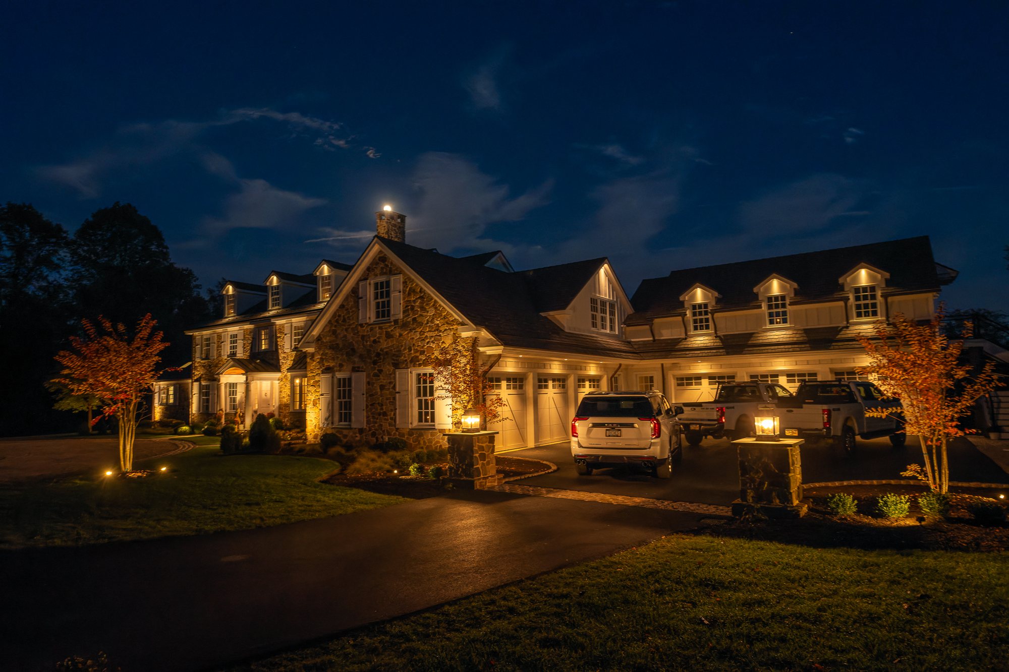 Stone home in Newtown Square, PA with warm landscape uplighting after dark by JHL Landscape Lighting